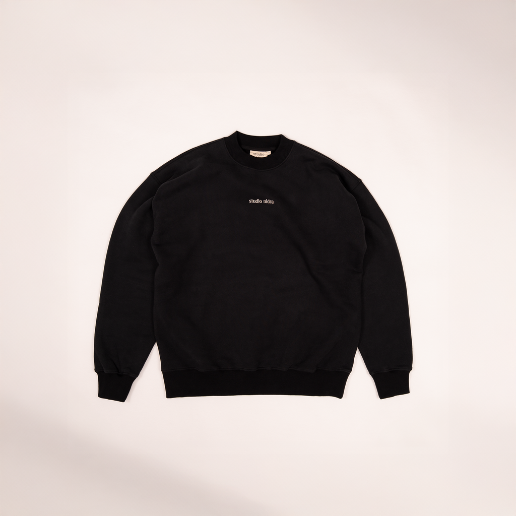Flat lay image of the black crewneck sweatshirt with studio nidra logo embroidery on a light background